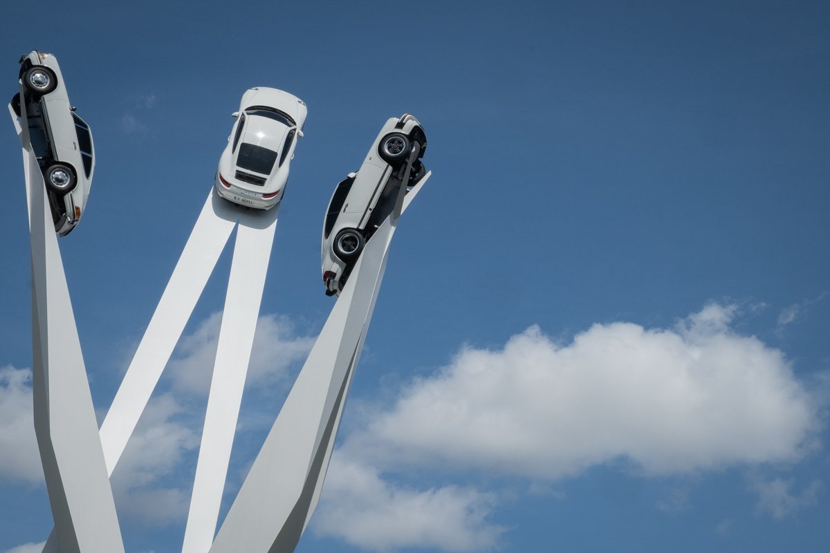 Sculpture with three Porsche cars rises toward the sky. 