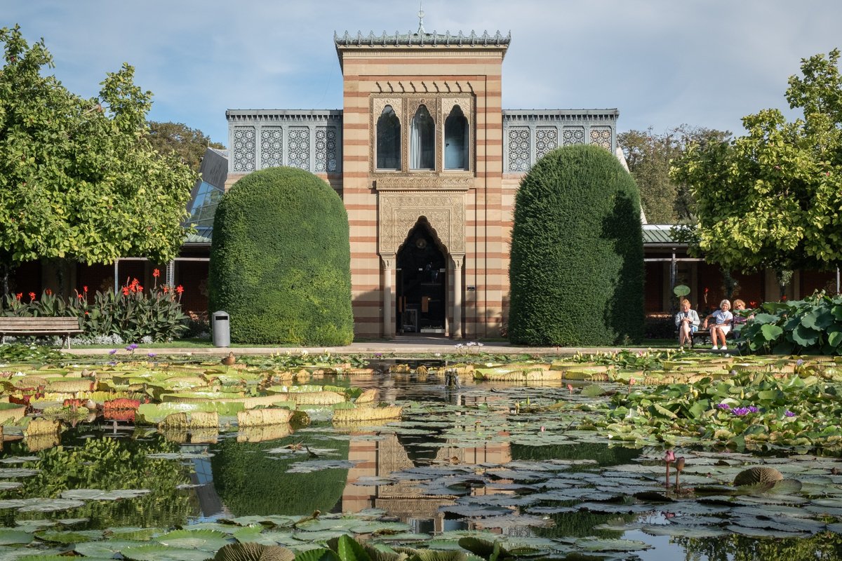 View of the Moorish Gardens at Wilhelma in Stuttgart Germany. A moorish building stands behind a pond covered in lily pads.