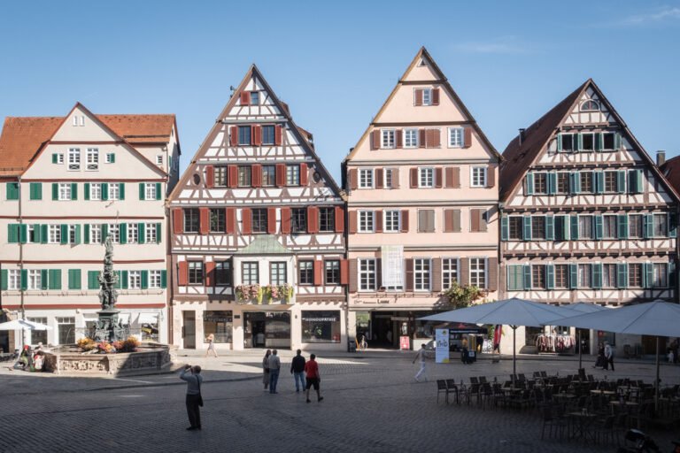 View of Fachwerk houses and the Neptune Fountain in Tübingen's central Marktplats. People walk through the central square.