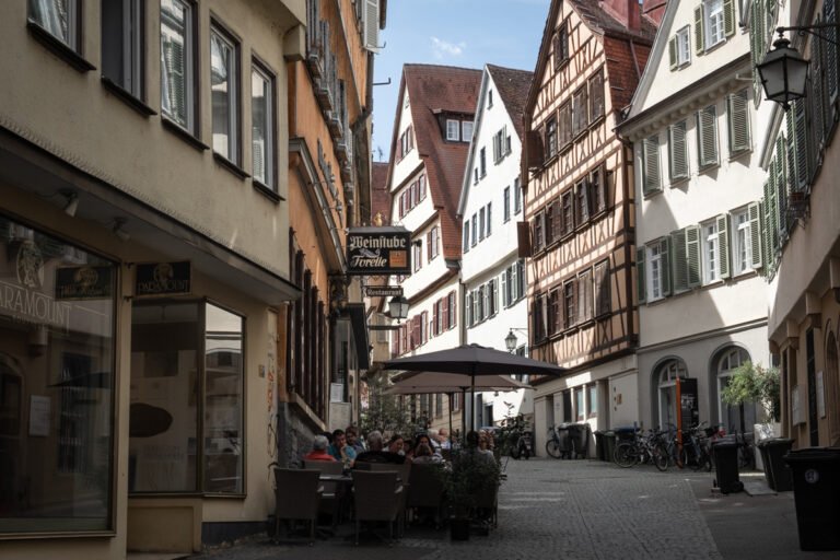View down a winding cobblestone street in Tübingen's Altstadt. Fachwerk houses. People dine at a cafe.